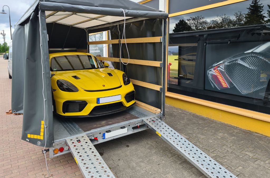 Professioneller Fahrzeugtransport - Gelber Porsche auf geschlossenem Transportanhänger