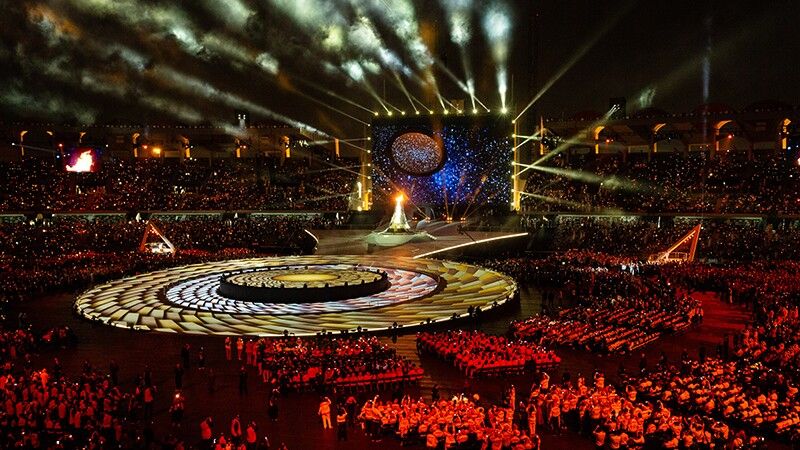 Special Olympics opening ceremony with circular stage design, dramatic lighting, and golden projection mapping