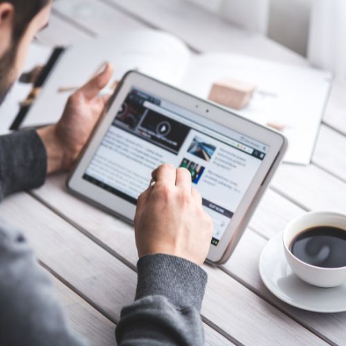 Professional reading news on tablet with coffee, representing media engagement and digital communication