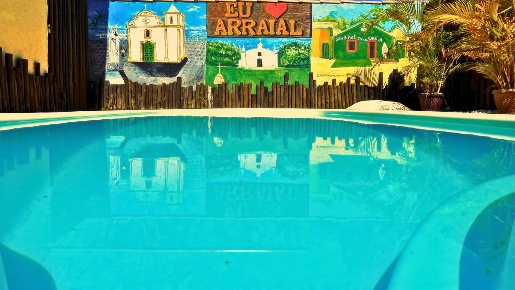 Piscina com mural 'EU ❤️ ARRAIAL' ao fundo e água cristalina