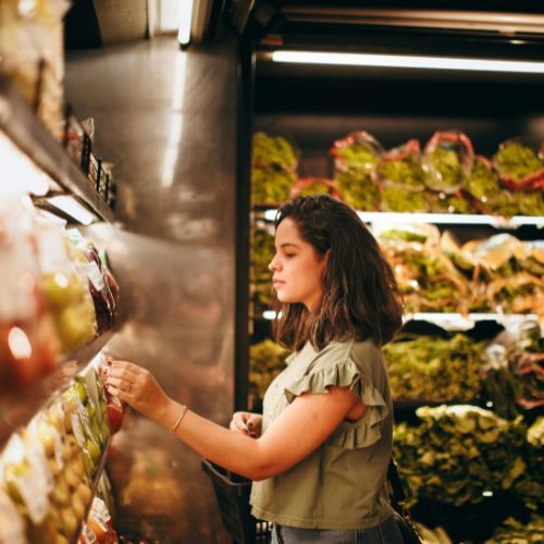 Woman shopping for fresh produce in grocery store, selecting vegetables from retail display