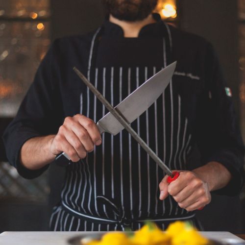 Professional chef sharpening knives representing precision and craftsmanship in food industry partnerships