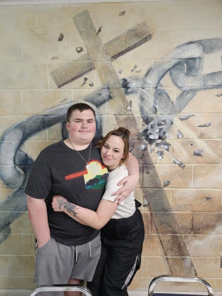 Embracing criminal justice participants in front of inspirational mural with cross and broken chains